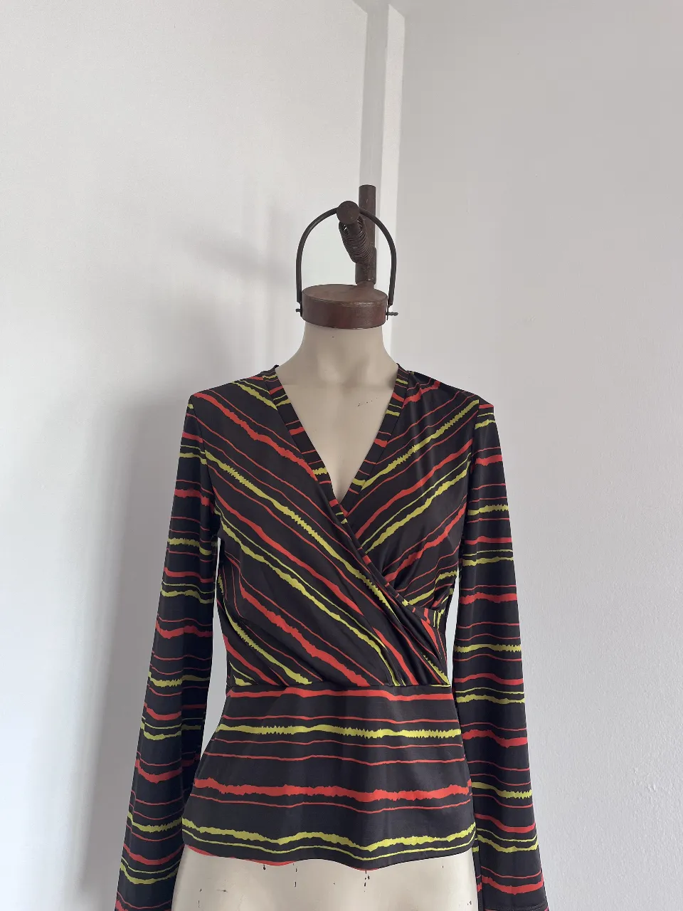 Blusa cruzada con estampado de rayas finas en negro, rojo y verde lima. Manga larga y escote en V pronunciado.
