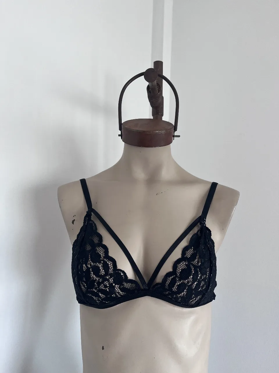 Corpiño de lencería negro de encaje, con tiras cruzadas en el escote y detalles de encaje festoneado. Ideal para sentirte sensual y cómoda. Tiene un detalle de costuras que se observa en la cuarta imagen. solucionable.