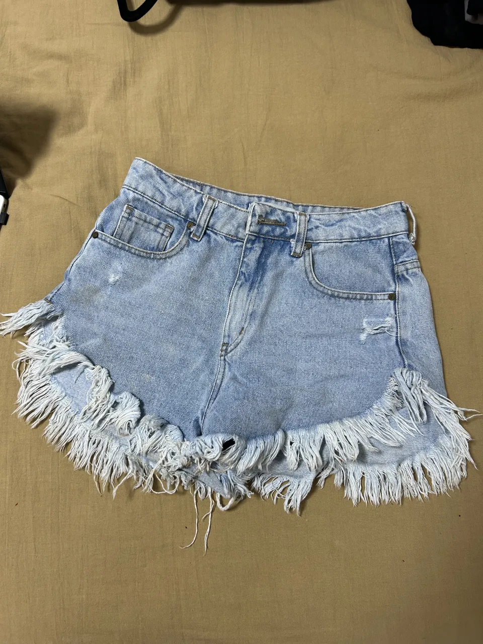 Shorts de jean tiro alto con roturas y flecos en el ruedo. Posee bolsillos delanteros y traseros.