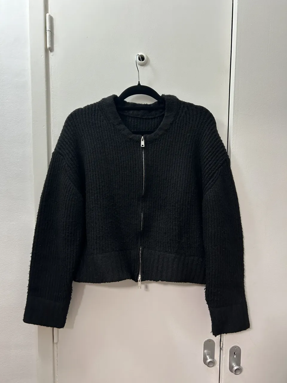 Buzo negro con cierre completo y cuello redondo. Tejido de punto con textura.