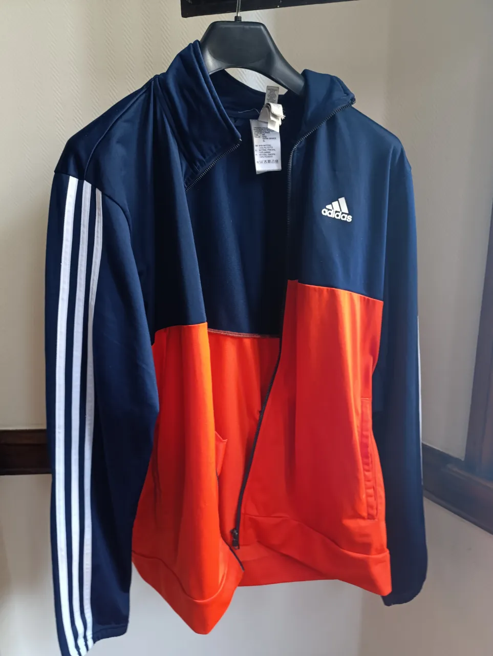 Buzo deportivo Adidas con cierre, de color azul y naranja. Con las tres tiras blancas características de la marca en la manga. Ideal para actividades deportivas o uso casual.