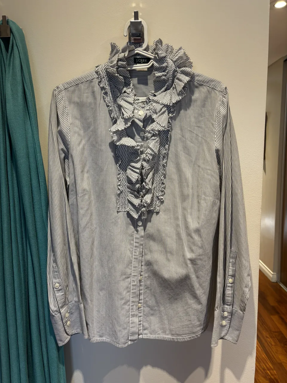 Camisa de vestir a rayas finas con volados y cuello alto. Un diseño delicado y con un toque romántico, ideal para un look elegante y sofisticado.