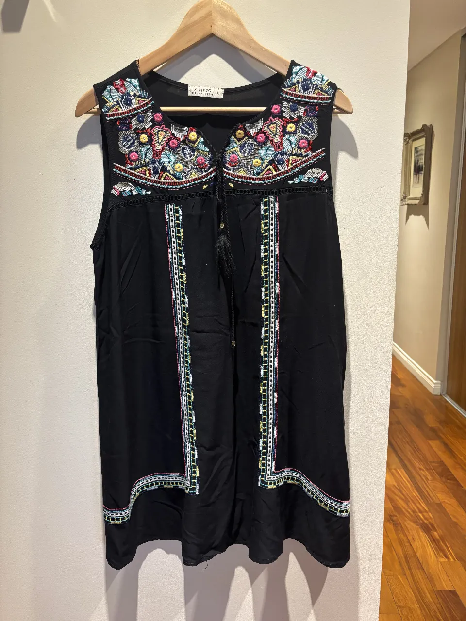 Musculosa negra con bordados coloridos en el cuello y detalles en los laterales. Posee un cordón con borla en la parte delantera para ajustar.