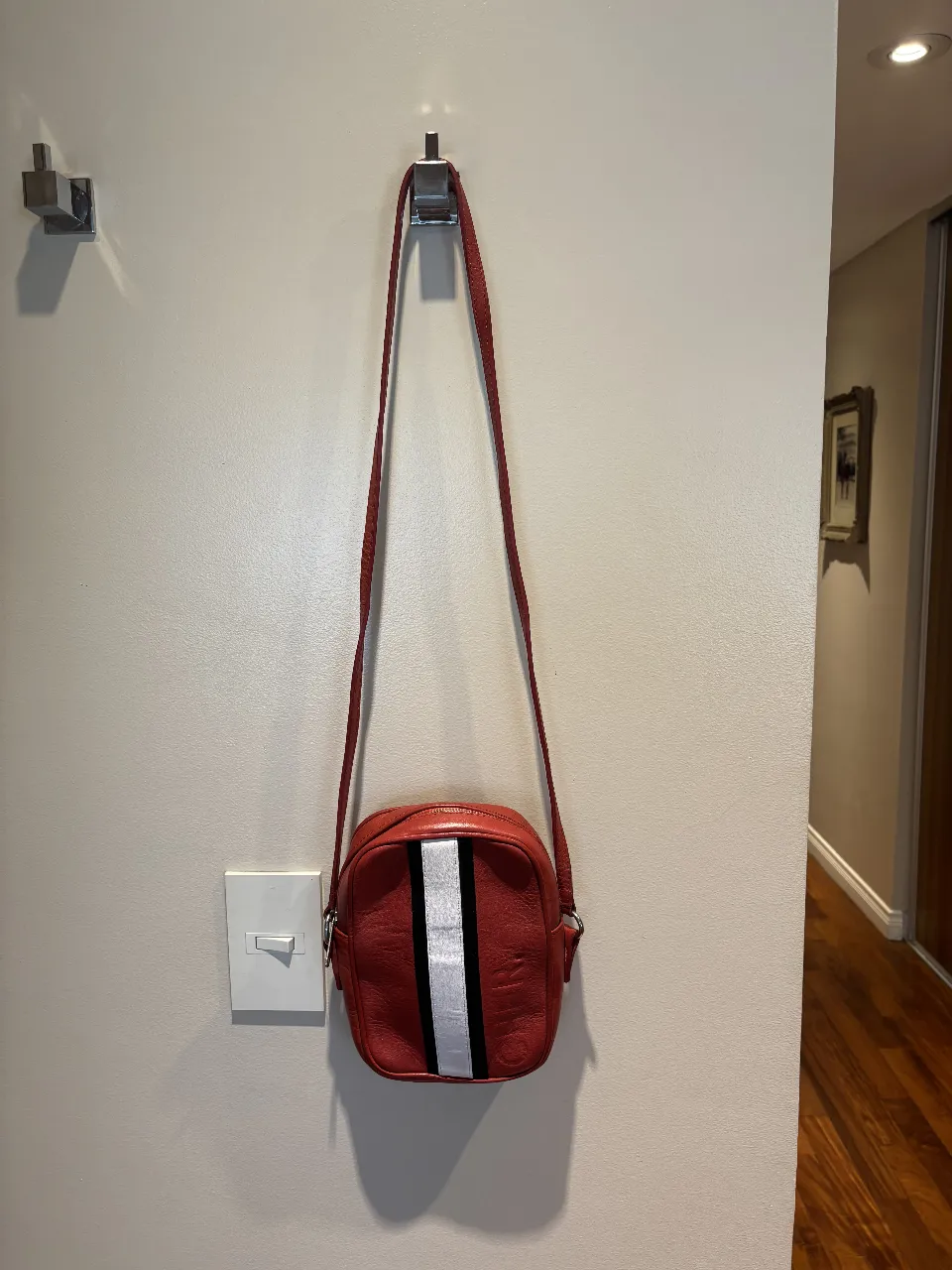 Cartera bandolera roja con detalles de franjas blancas y negras. Ideal para el día a día o para un look casual y deportivo.