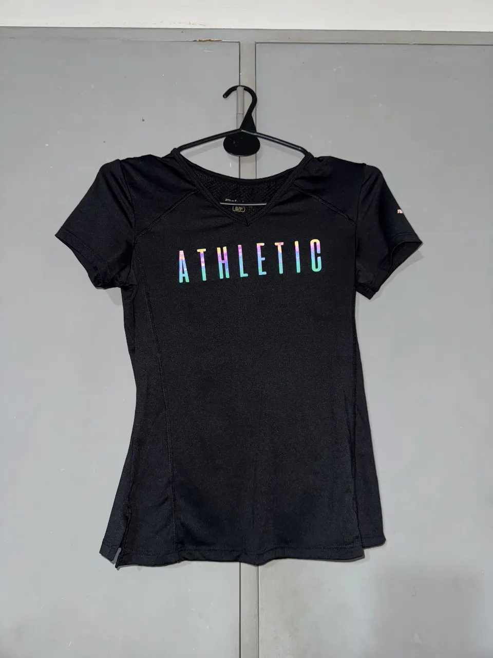 Remera deportiva negra para mujer con estampado "ATHLETIC" iridiscente. Diseño de manga corta y ajuste entallado, ideal para actividades físicas. Confeccionada con tejido técnico transpirable. Talle S o M