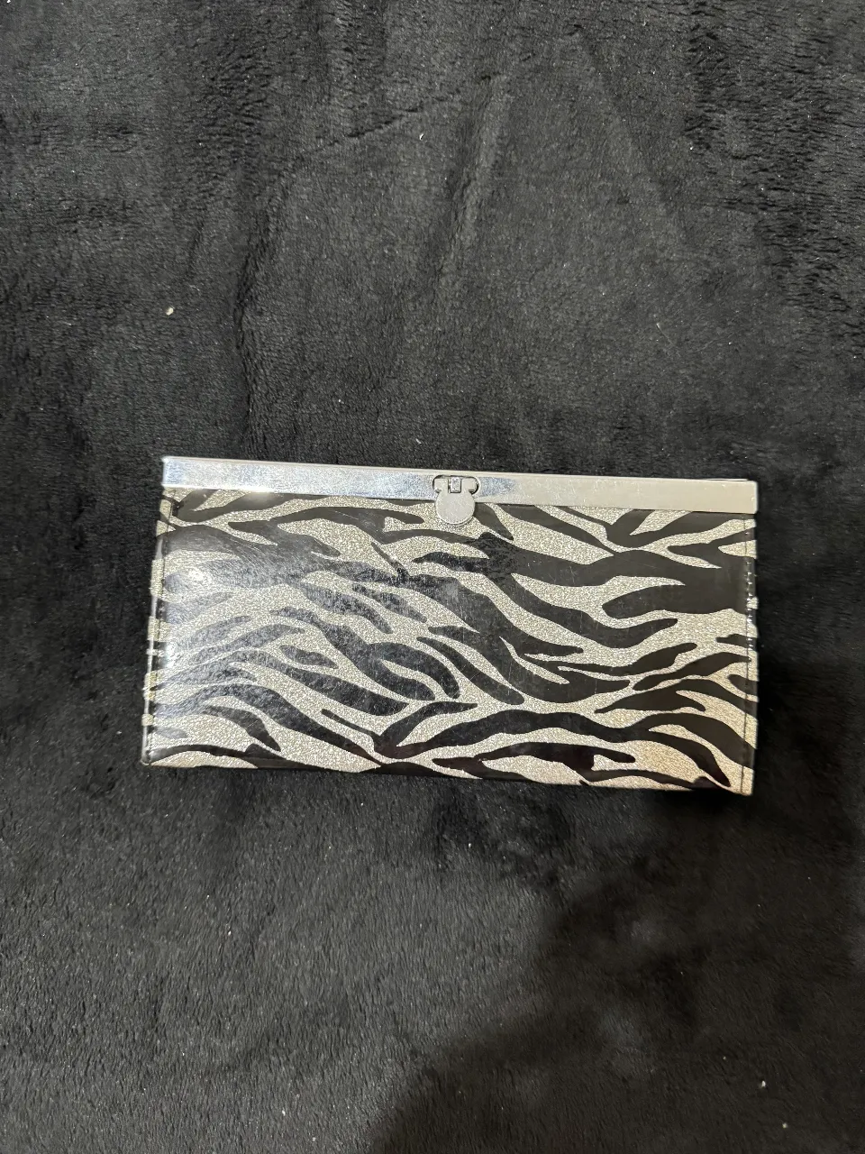 Billetera de mujer con estampado de cebra en tonos plateados y negros. Diseño rectangular con cierre metálico y compartimentos internos.