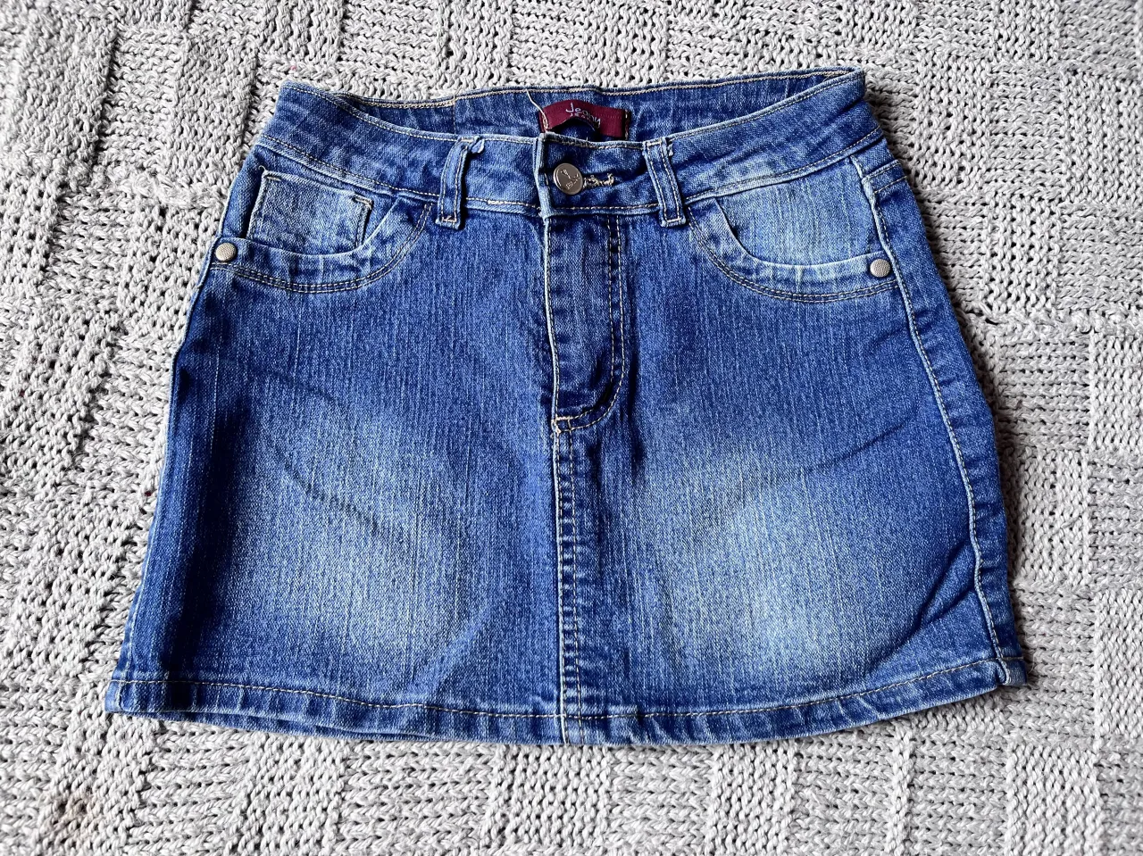 Pollera de jean tiro alto, con tachas en los bolsillos traseros. Un clásico que no puede faltar en tu guardarropa, ideal para combinar con todo.