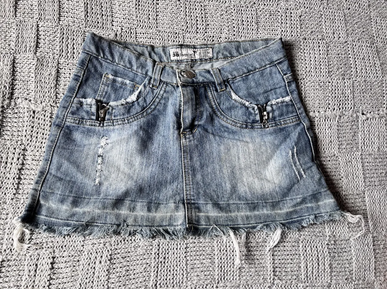 Pollera de jean tiro alto, con roturas y detalles deshilachados en los bordes y bolsillos. Posee tachas y cierres decorativos en los bolsillos delanteros. Un modelo súper canchero y moderno, ideal para armar looks urbanos y descontracturados.