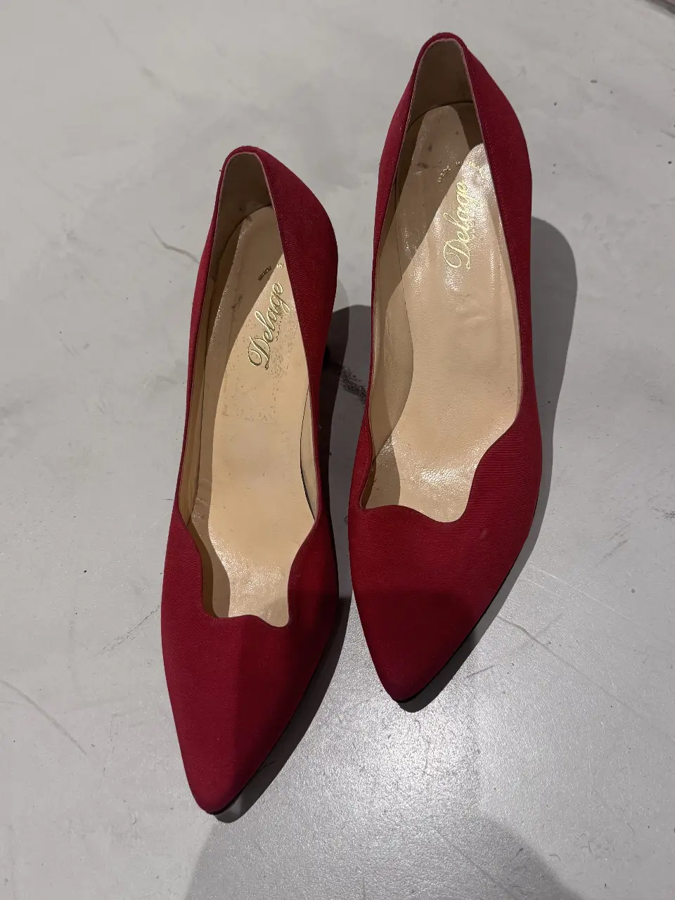 Elegantes zapatos de tacón alto rojos de la marca Delage. Ideales para eventos formales o fiestas, estos zapatos de gamuza presentan un diseño clásico con un toque vintage.