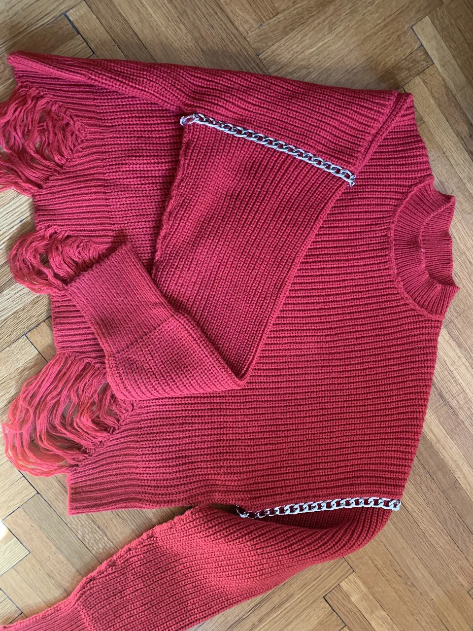 Sweater largo de punto rojo con flecos y detalles de cadena plateada. Ideal para un look moderno y abrigado. Talle S.