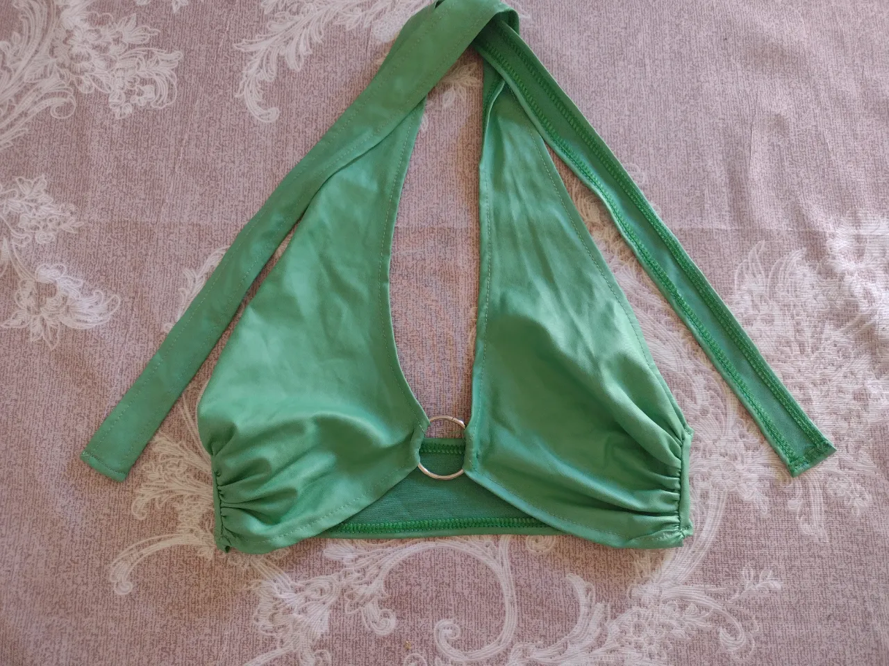 Top de bikini color verde con detalle de aro metálico en el centro. Breteles finos para atar en cuello y espalda.