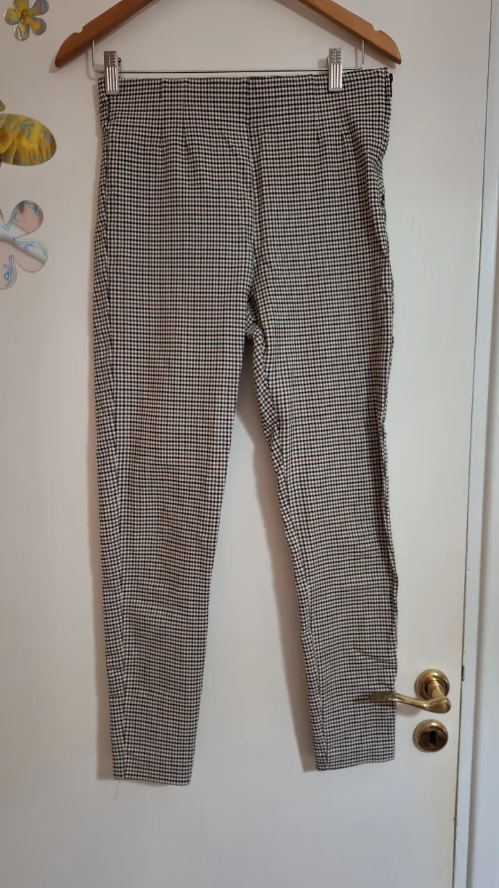 Pantalón a cuadros escoceses en tonos marrón, negro y blanco. Posee bolsillos.