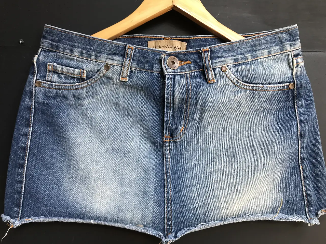 Minifalda de jean azul Sarkany. ideal para un look casual y moderno. Confeccionada en tela de jean resistente, esta falda corta es perfecta para el verano. Cuenta con detalles clásicos como bolsillos y botón.