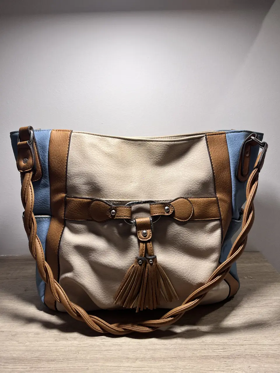 Cartera Rosetti de hombro, con diseño en dos tonos, detalles en marrón y celeste. Posee un cierre superior y un detalle de borlas.