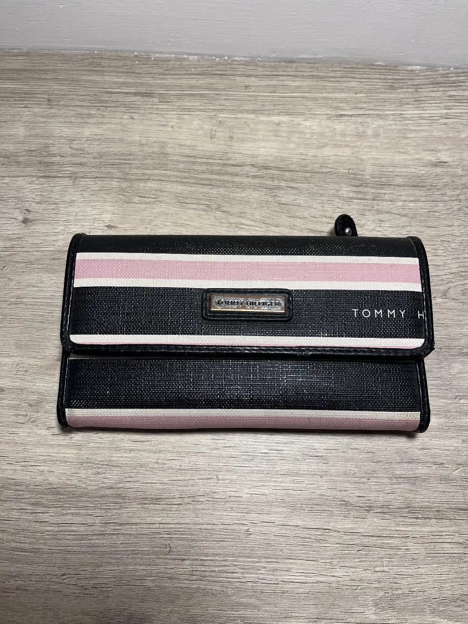 Billetera Tommy Hilfiger de mujer, con diseño a rayas en rosa y negro. Cuenta con cierre y varios compartimentos internos para tarjetas y billetes. Ideal para organizar tus pertenencias con estilo. Tiene un tajo en la parte trasera. 