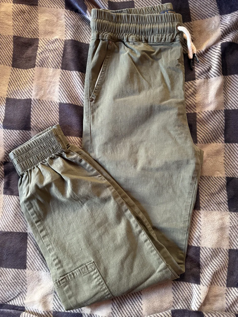 Pantalón cargo de color verde. Posee cintura con elástico y cordón blanco. Tiene bolsillos laterales y bolsillos cargo en los laterales de las piernas. La parte inferior de las piernas es ajustada con elástico.