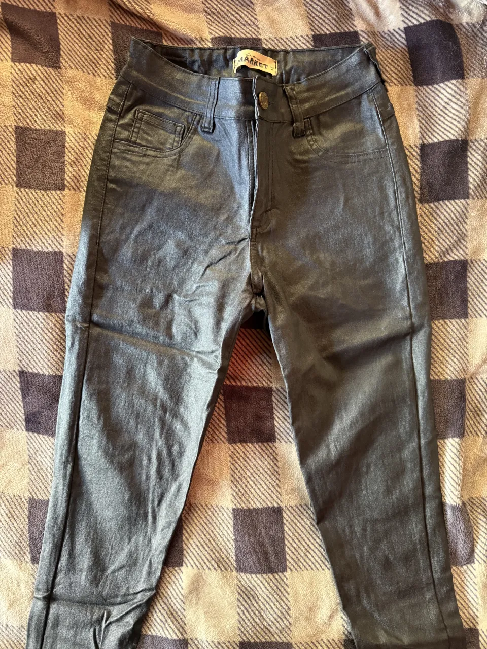 Pantalón de cuero sintético negro, con cierre y botón en la cintura. Posee bolsillos delanteros y traseros.