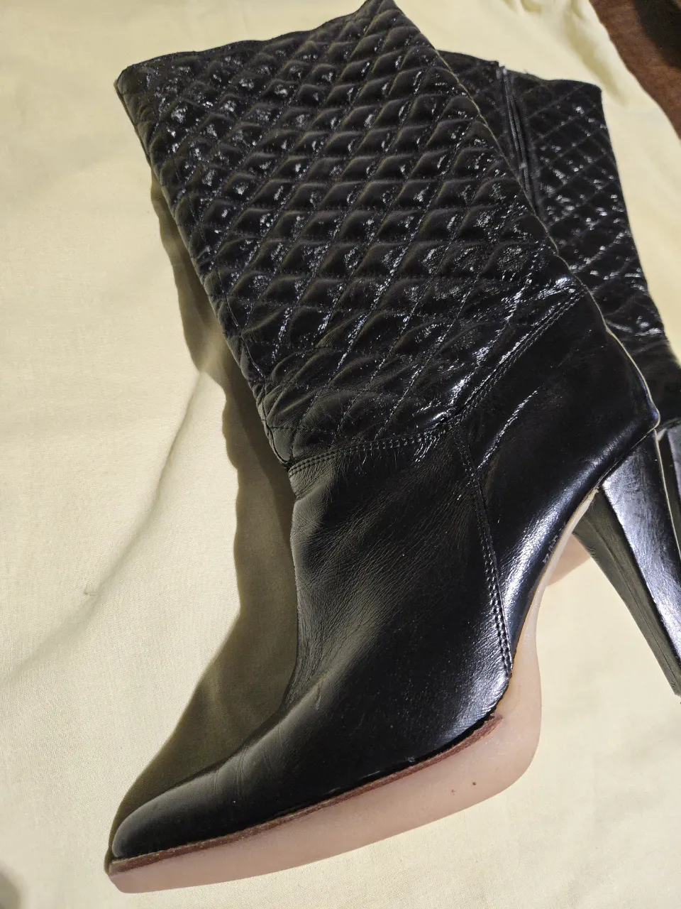 Botas negras de caña alta, con taco y punta fina. La parte superior de la caña tiene un diseño acolchado en rombos. La suela es de color claro.