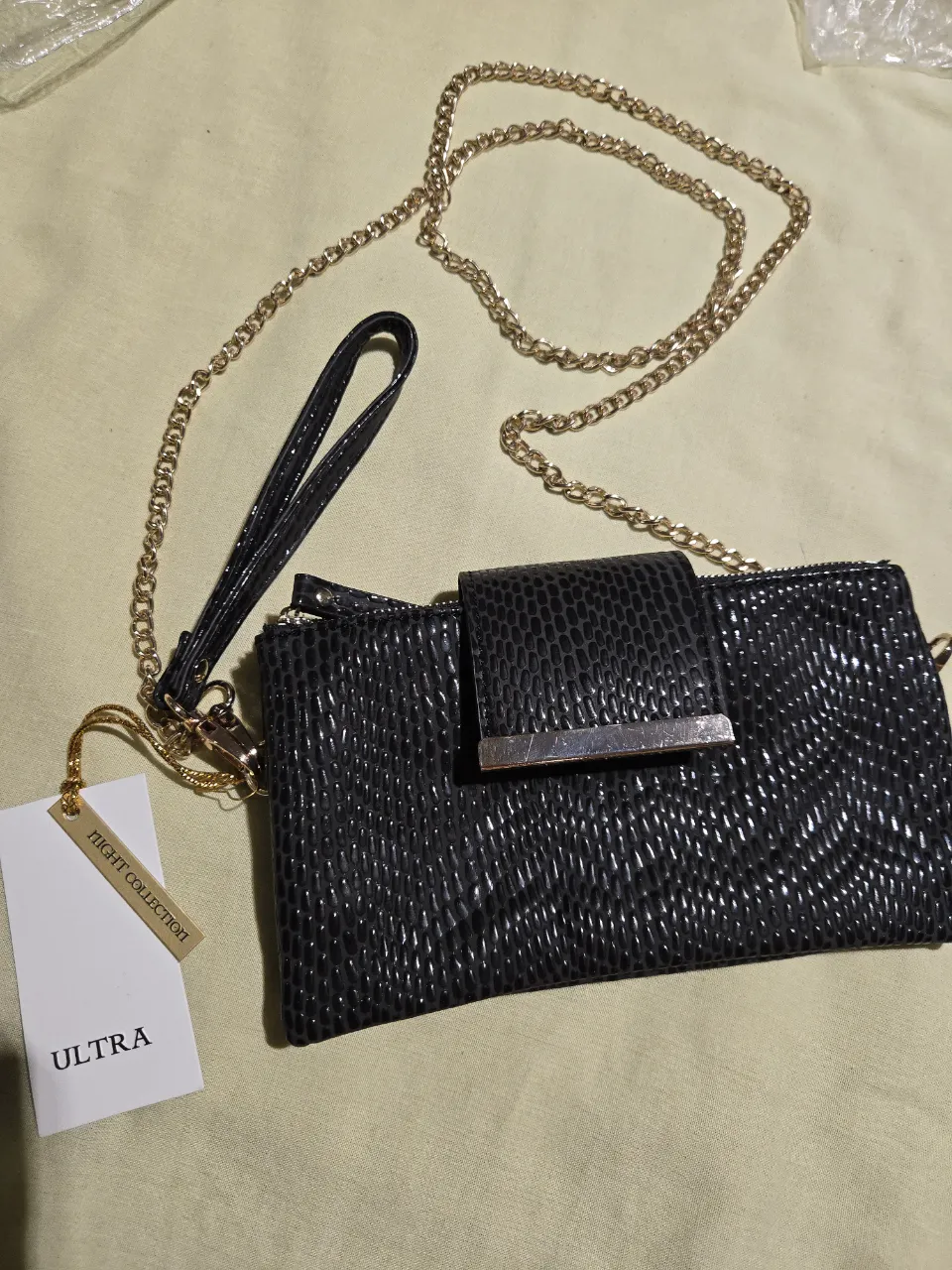 Cartera negra con textura, cadena dorada y muñequera. Tiene varios compartimentos internos con cierre.