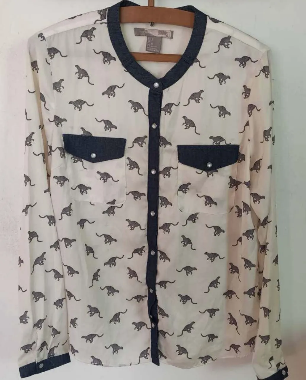 Camisa blanca estampada con leopardos grises. Cuello redondo con detalle en tela de jean. Dos bolsillos en el frente. Manga larga. Ideal para un look casual y canchero.