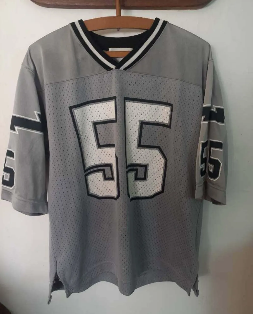 Remera de fútbol americana gris con el número 55 en blanco. Cuello en V con detalles en negro y blanco. Ideal para un look deportivo y casual.