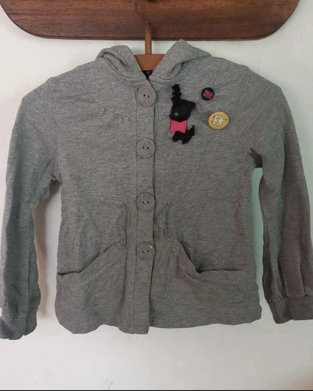 Campera gris con capucha, ideal para niñas. Posee botones grandes al frente y dos bolsillos amplios. Tiene apliques divertidos en el frente que le dan un toque único. Único detalle un pequeño desgaste en uno de sus botones (se puede ver en la última foto). Perfecta para el día a día o para salir a jugar.
