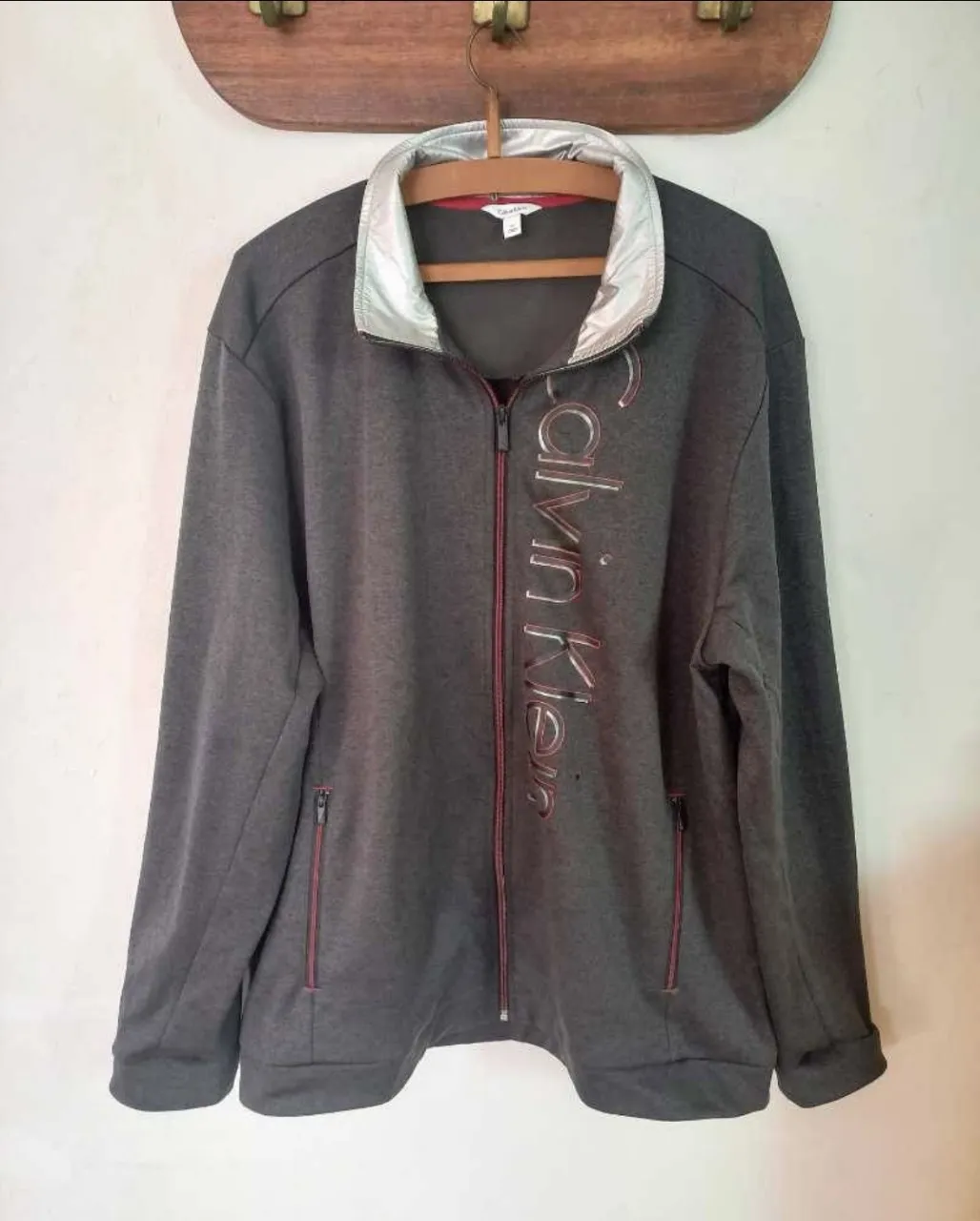 Buzo gris con cierre completo y cuello plateado. Posee logo de la marca en el frente y bolsillos con cierre. Ideal para un look casual y deportivo.