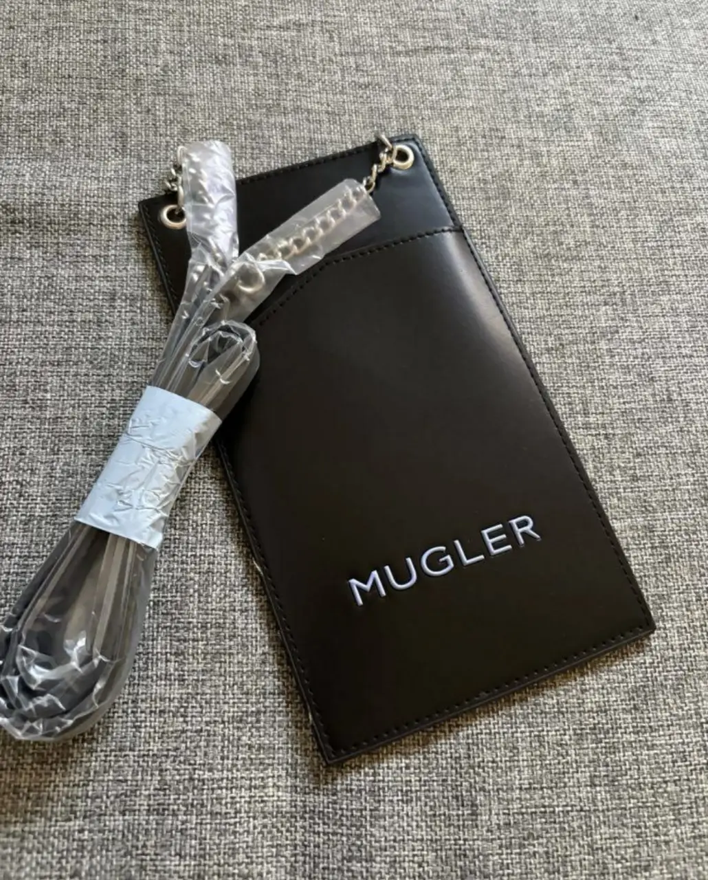 Porta celular Mugler negra con correa para colgar. Diseño minimalista y elegante, ideal para llevar lo esencial con estilo. Pequeños detalles en los costados que se muestran en las fotos. 