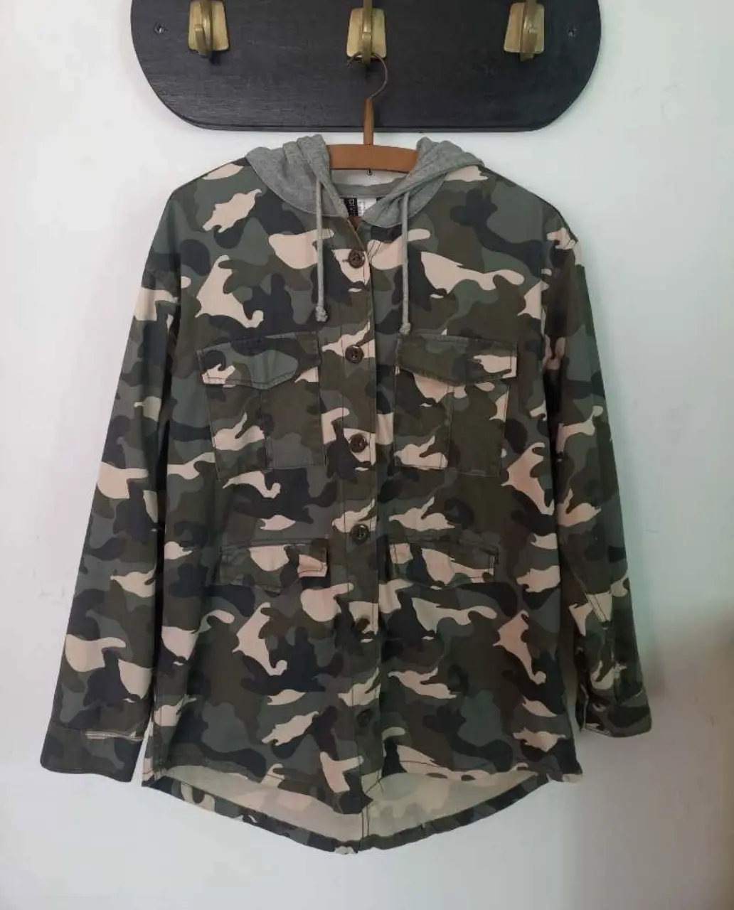 Campera con capucha de camuflaje, con botones. Posee capucha gris y bolsillos delanteros. Ideal para un look casual y urbano.