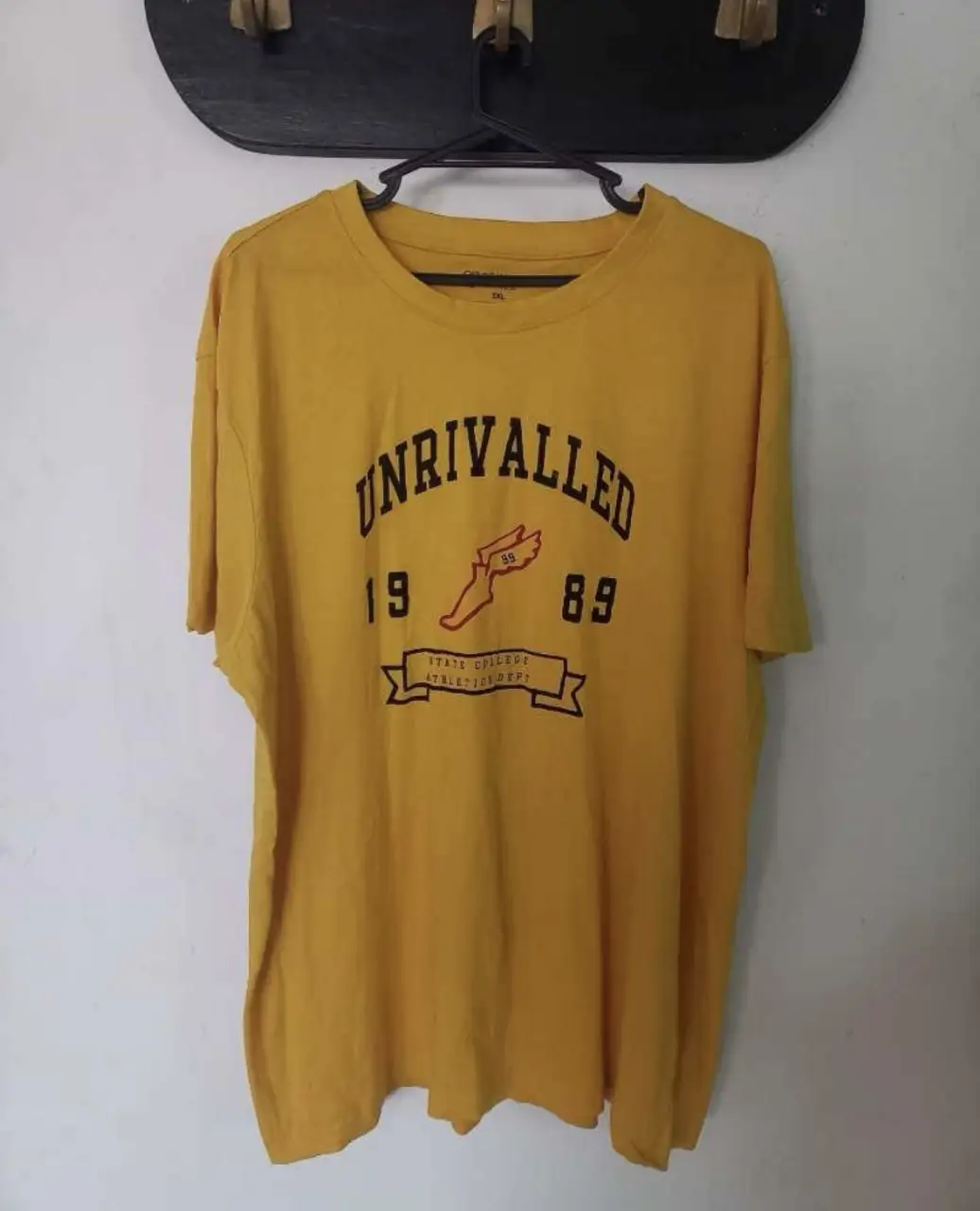 Remera amarilla de manga corta con estampado "UNRIVALLED 1989" en el frente. Talle 2XL, ideal para un look casual y cómodo.