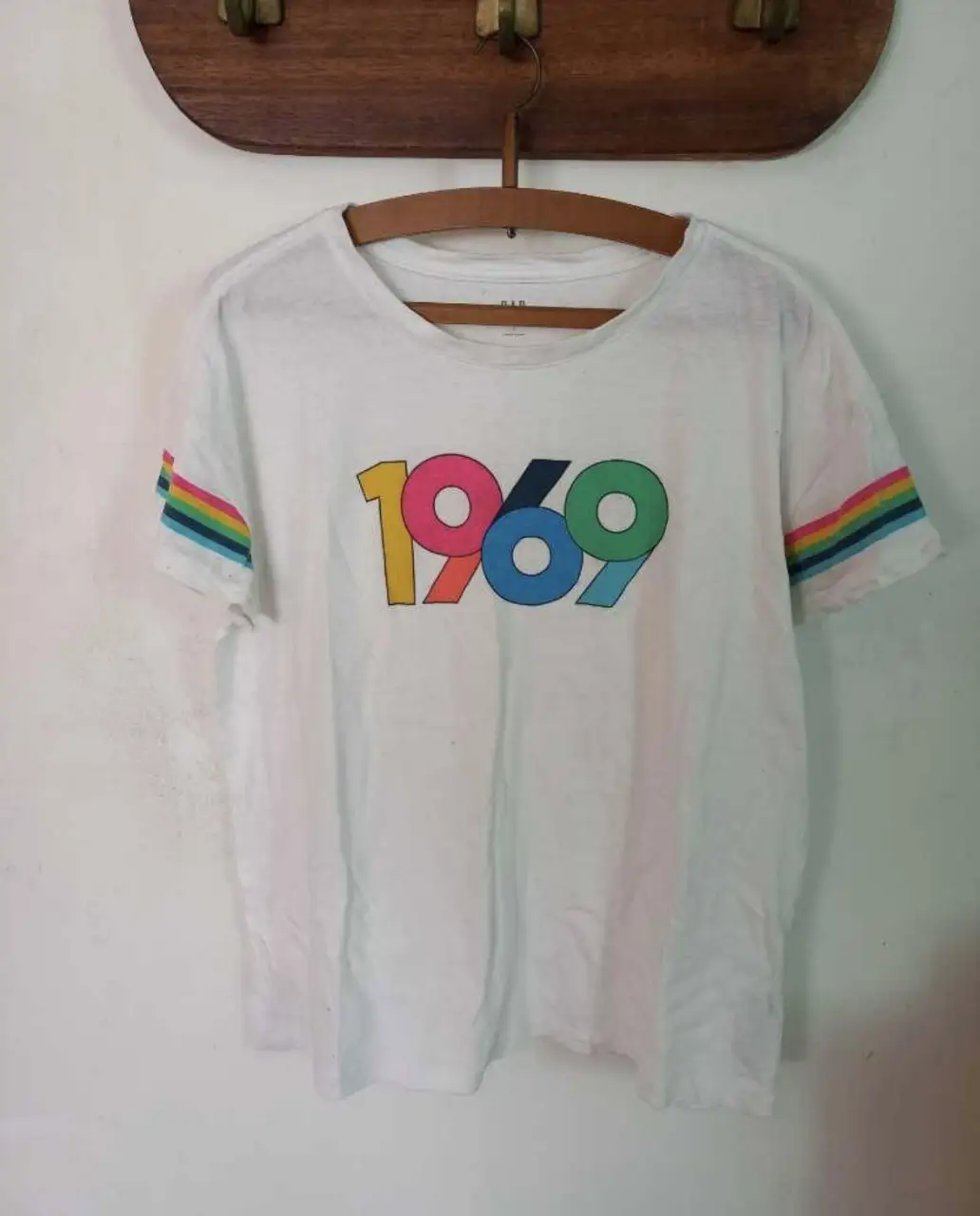 Remera blanca con estampado "1969" en colores y detalles de rayas en las mangas. Ideal para un look casual y retro.