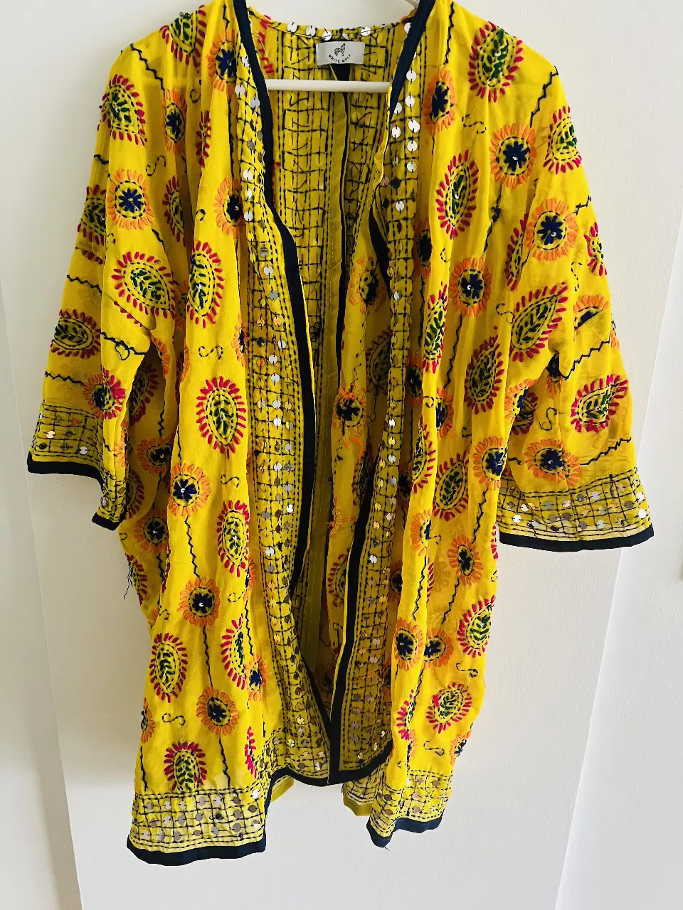 Kimono de la India amarillo con bordados florales en tonos rojo, naranja y azul. Detalles de lentejuelas plateadas. Estilo boho y artesanal, ideal para un look casual y de verano.