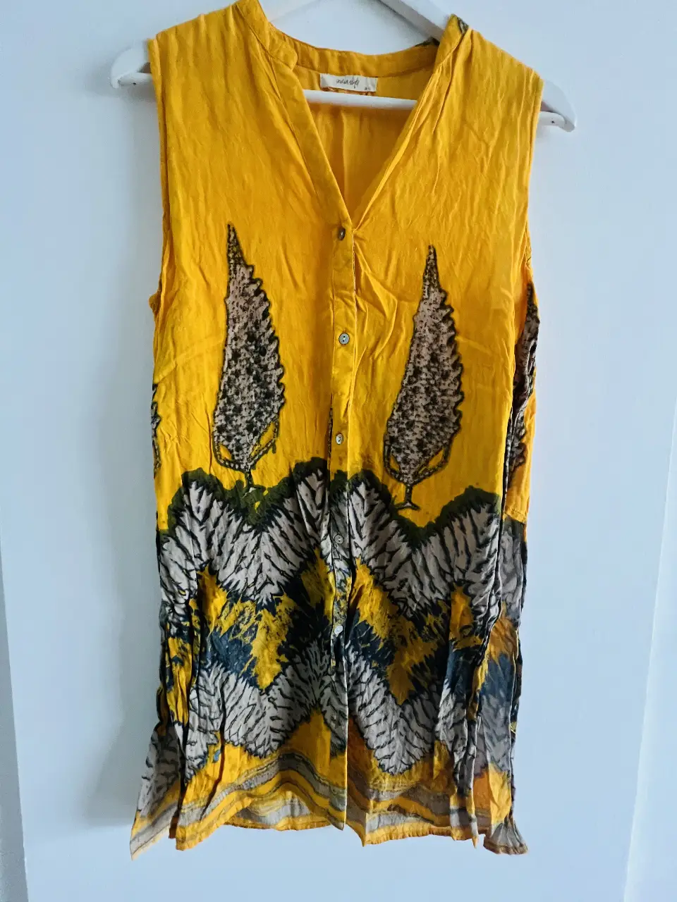Blusa sin mangas de color amarillo mostaza con estampado de árboles en tonos tierra y detalles en la parte inferior. Ideal para un look fresco y bohemio.