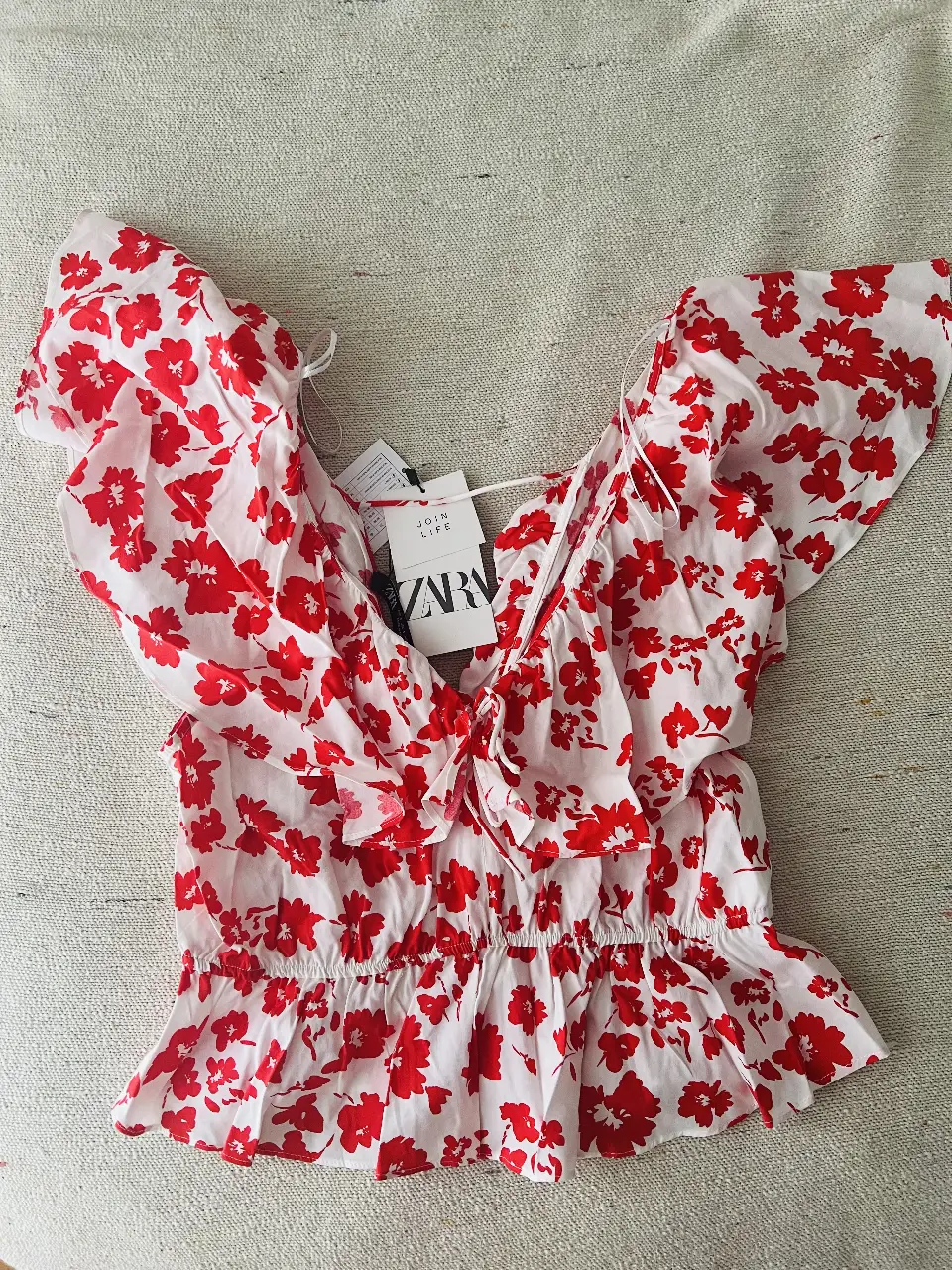 Blusa de mujer con estampado floral en rojo y blanco, con volados en las mangas y detalle de lazo en el escote. Ideal para un look fresco y femenino.