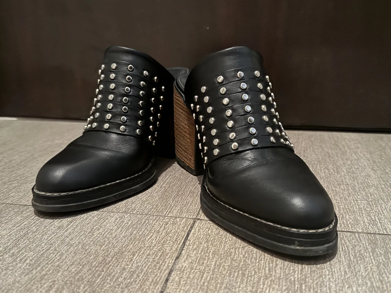 Zuecos negros de cuero con detalles de tachas plateadas. Tienen taco de madera y plataforma. Ideales para un look moderno y canchero.