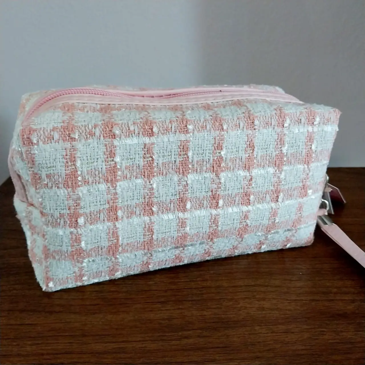 Neceser rectangular de tela tipo tweed en tonos rosa y blanco. Cuenta con cierre y manija lateral. Ideal para guardar cosméticos y accesorios.