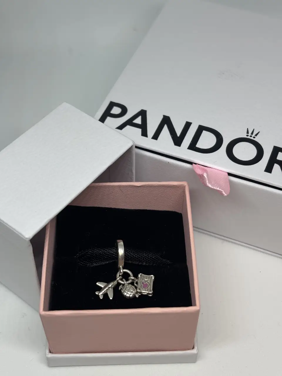 Dije colgante de la marca Pandora, con diseño de avión, globo terráqueo y un pequeño corazón rosa. Ideal para amantes de los viajes.