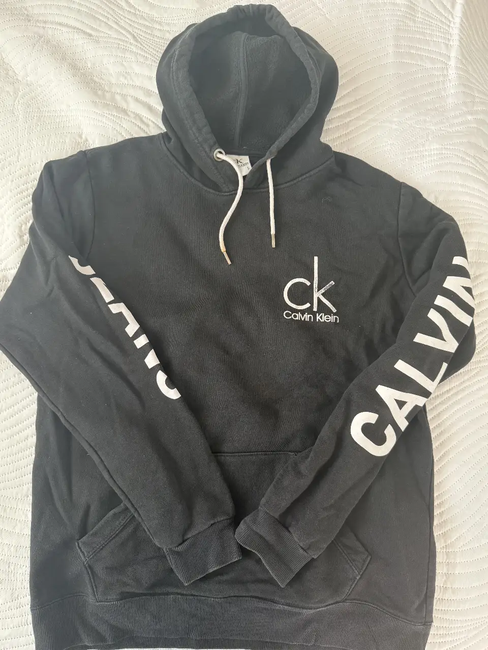 Buzo canguro negro de Calvin Klein con logo blanco en el pecho y en la manga. Ideal para un look casual y cómodo. para hombre y mujer 