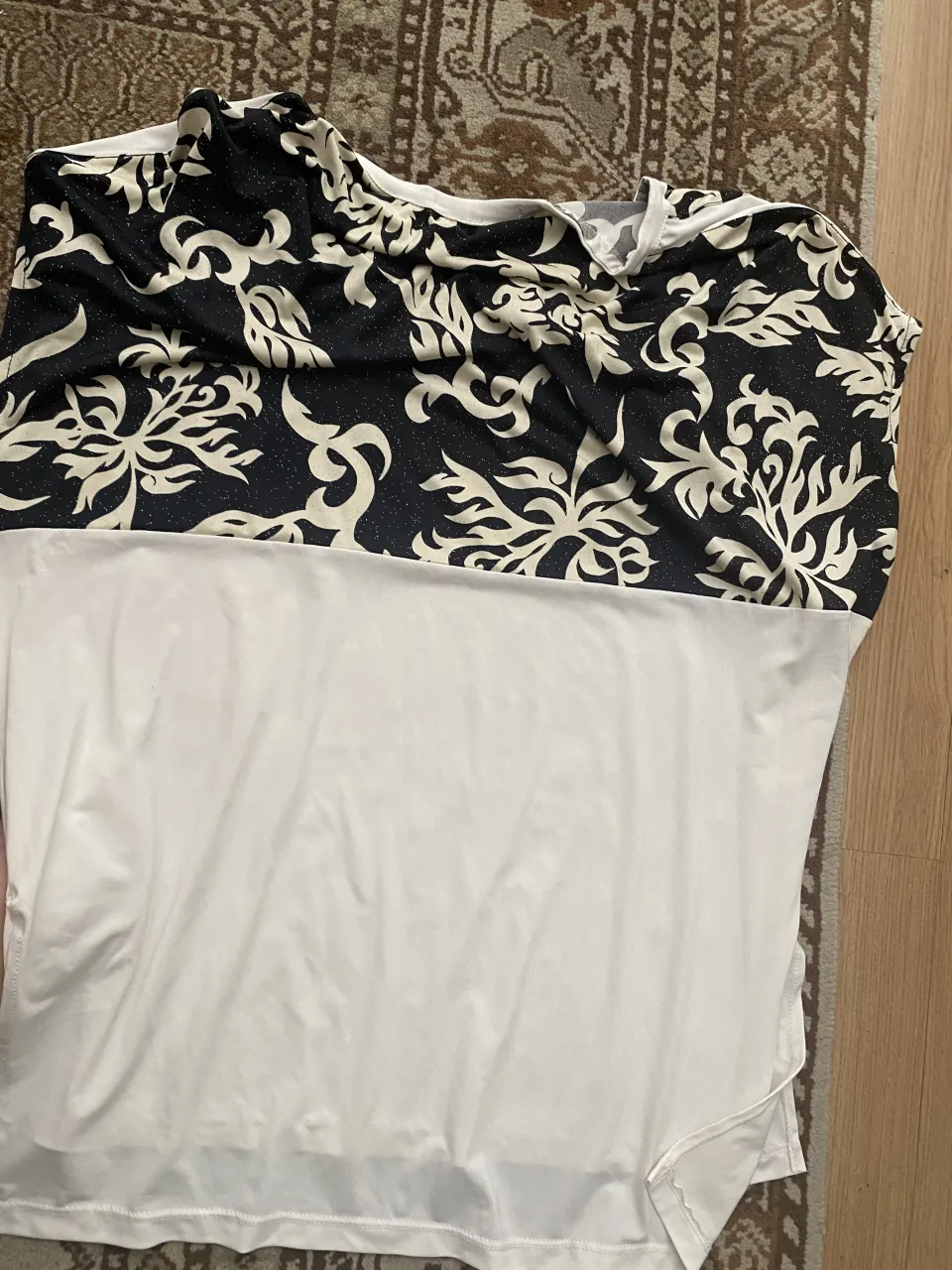 Remera manga corta con estampa floral en blanco y negro. La parte superior tiene un diseño intrincado y la parte inferior es lisa en blanco. Ideal para un look casual y moderno.