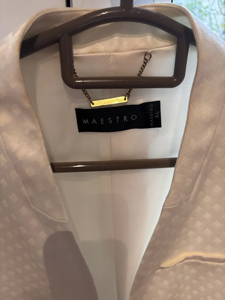 Blazer blanco con textura de rombos pequeños. Tiene un broche dorado en la parte superior y un bolsillo en el frente.