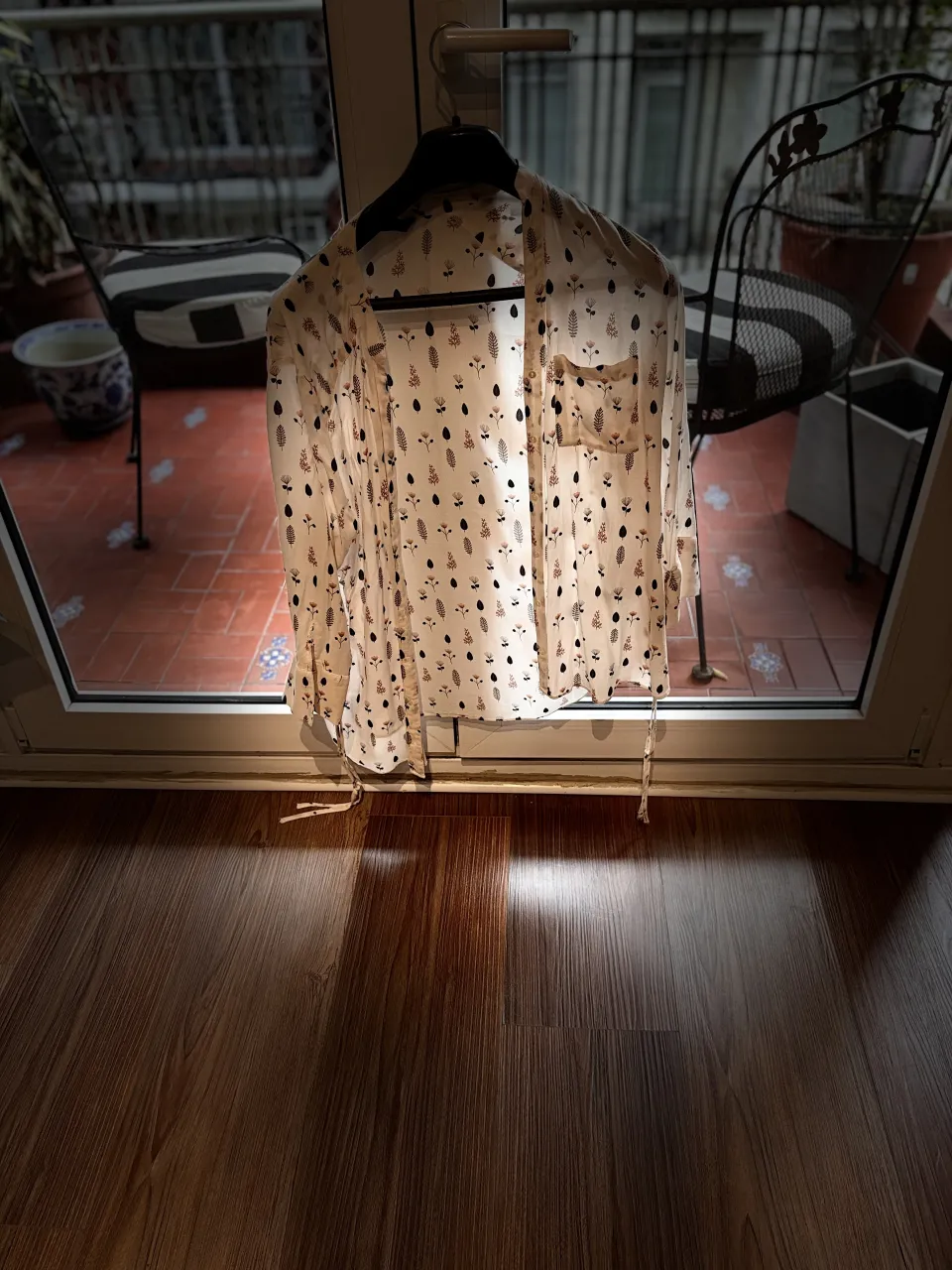 Camisa blanca con estampado de flores y hojas en tonos negro, rosa y verde. Posee un bolsillo en el frente izquierdo y botones nacarados.