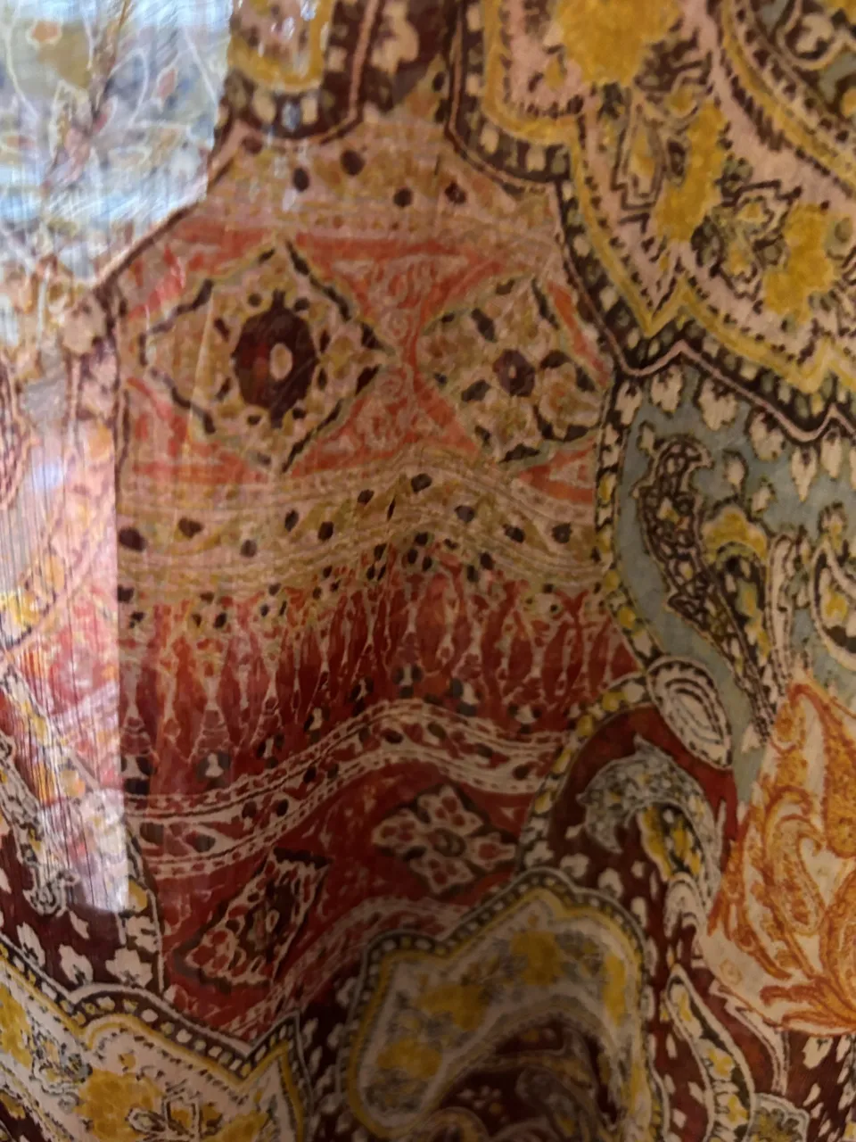 Blusa estampada con motivos florales y paisleys en tonos tierra, rojo, amarillo y azul. Posee cuello redondo y mangas largas. La tela es liviana y vaporosa.