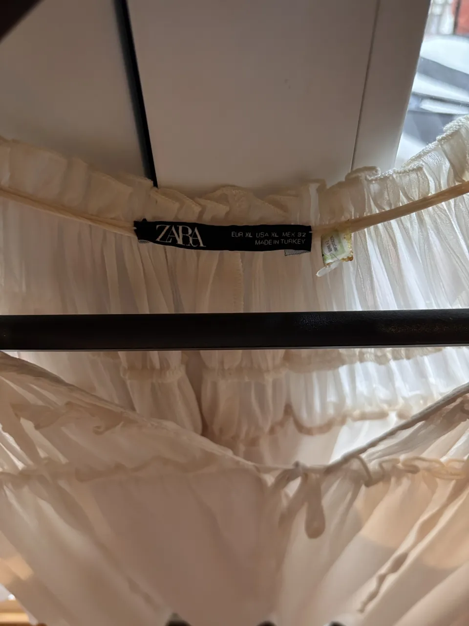 Blusa blanca con cuello redondo, detalles de volados y lazo en el escote. Mangas cortas.