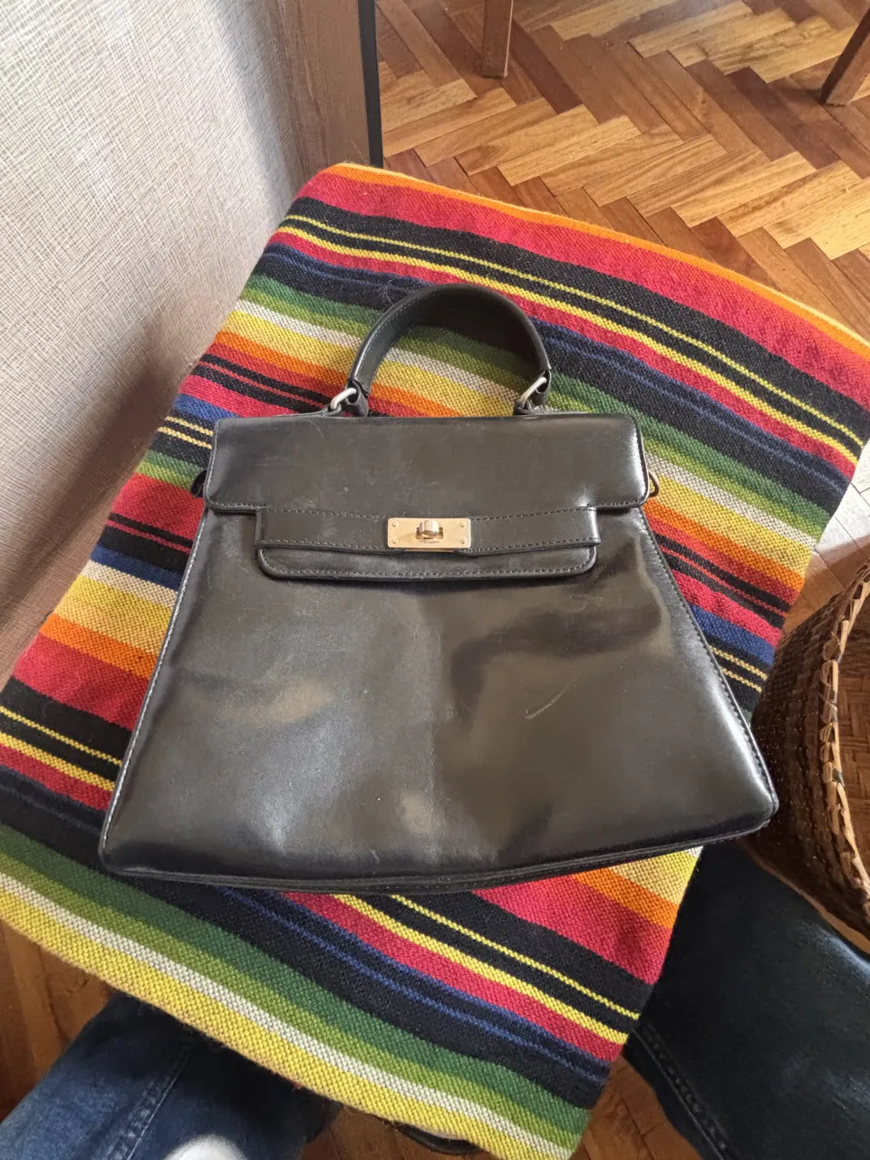 Cartera negra de cuero con tapa y cierre metálico dorado. Posee manija superior.