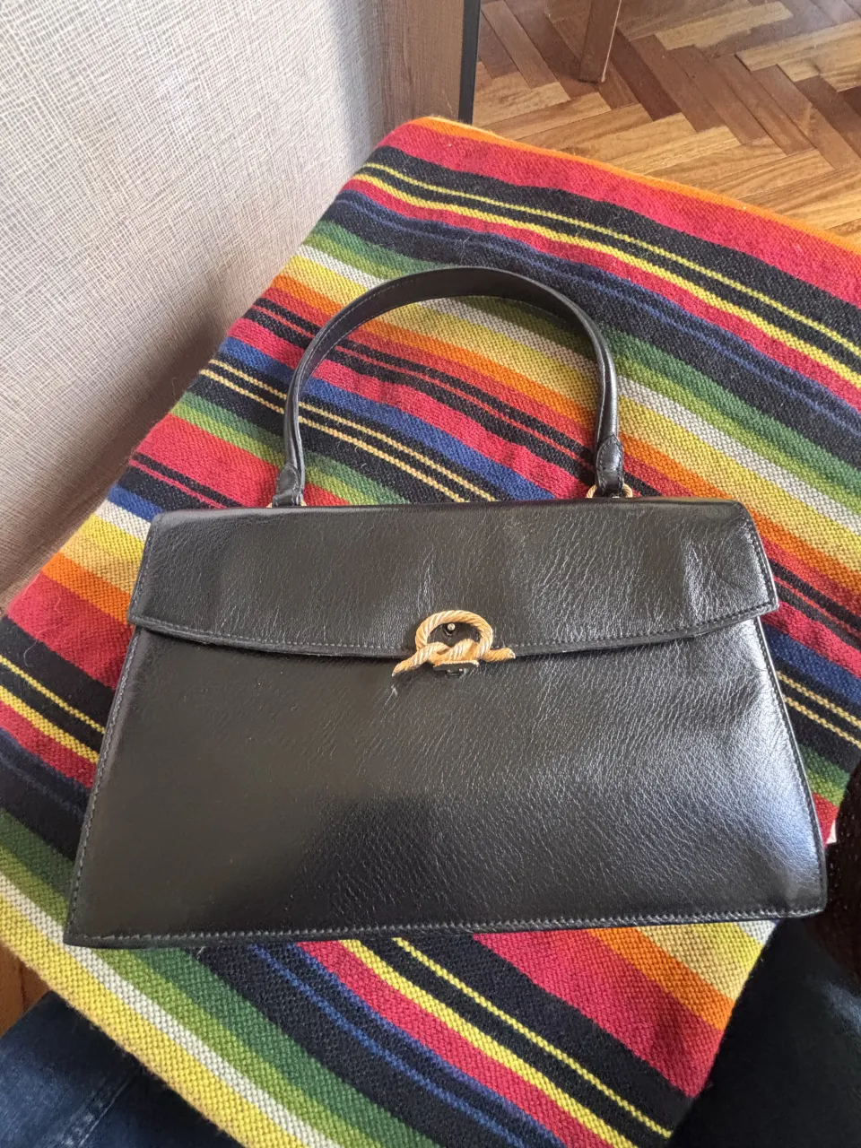 Cartera negra con cierre dorado y detalle de nudo.