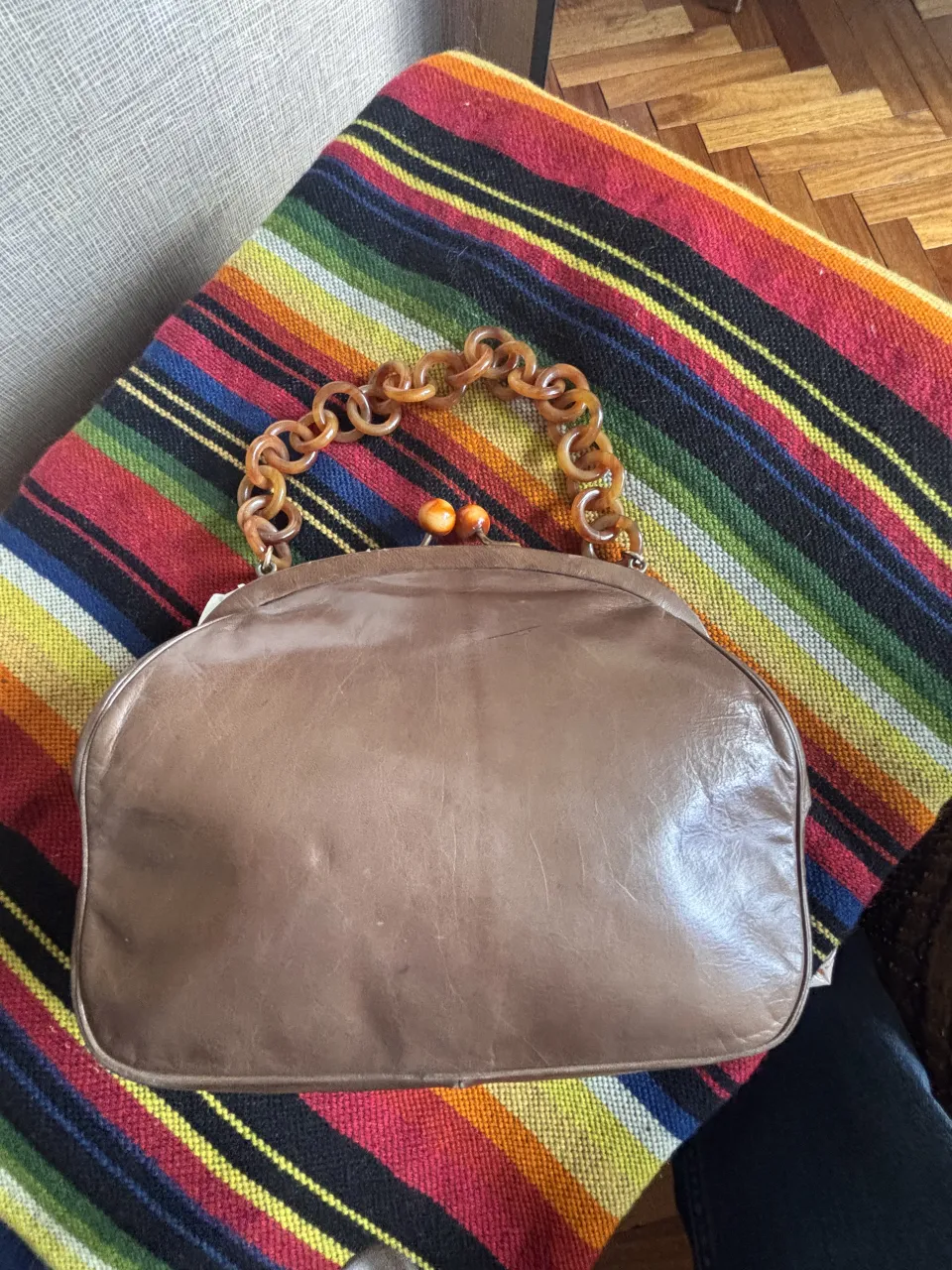 Cartera de cuero color marrón con manija de acrílico estilo carey. Cierre metálico con dos bolitas naranjas.