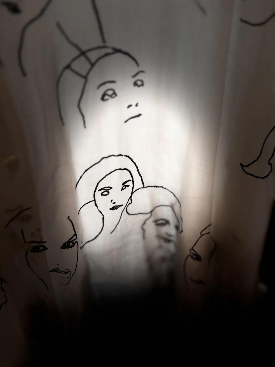 Camisa blanca con estampa de rostros dibujados en negro. Tiene mangas largas y botones al frente.