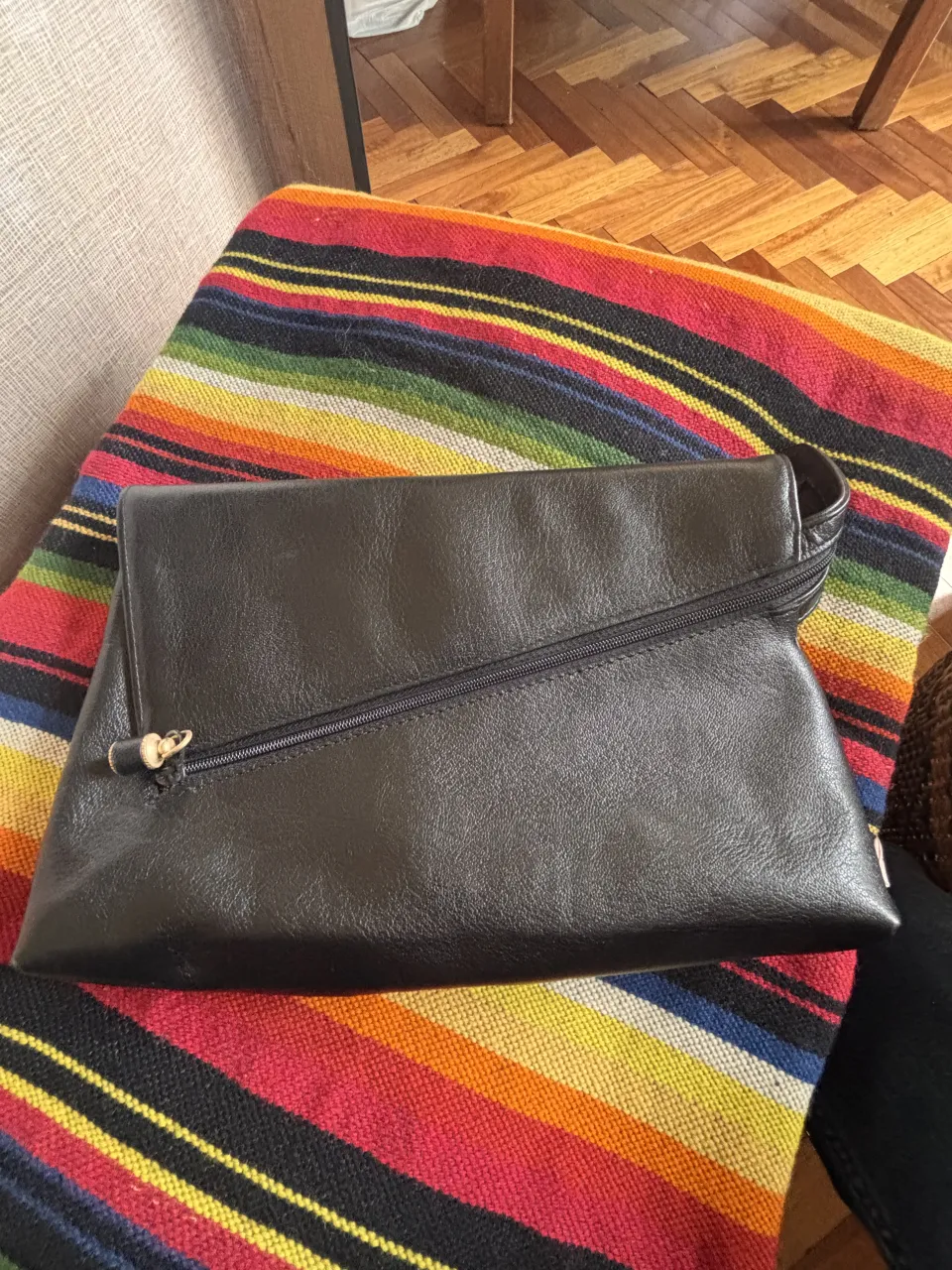 Cartera negra de cuero con cierre diagonal y detalle de madera en el tirador.