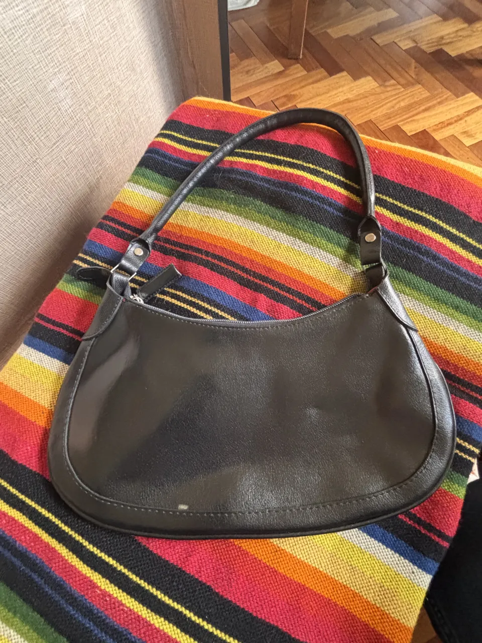Cartera negra de cuero sintético con correa de mano.