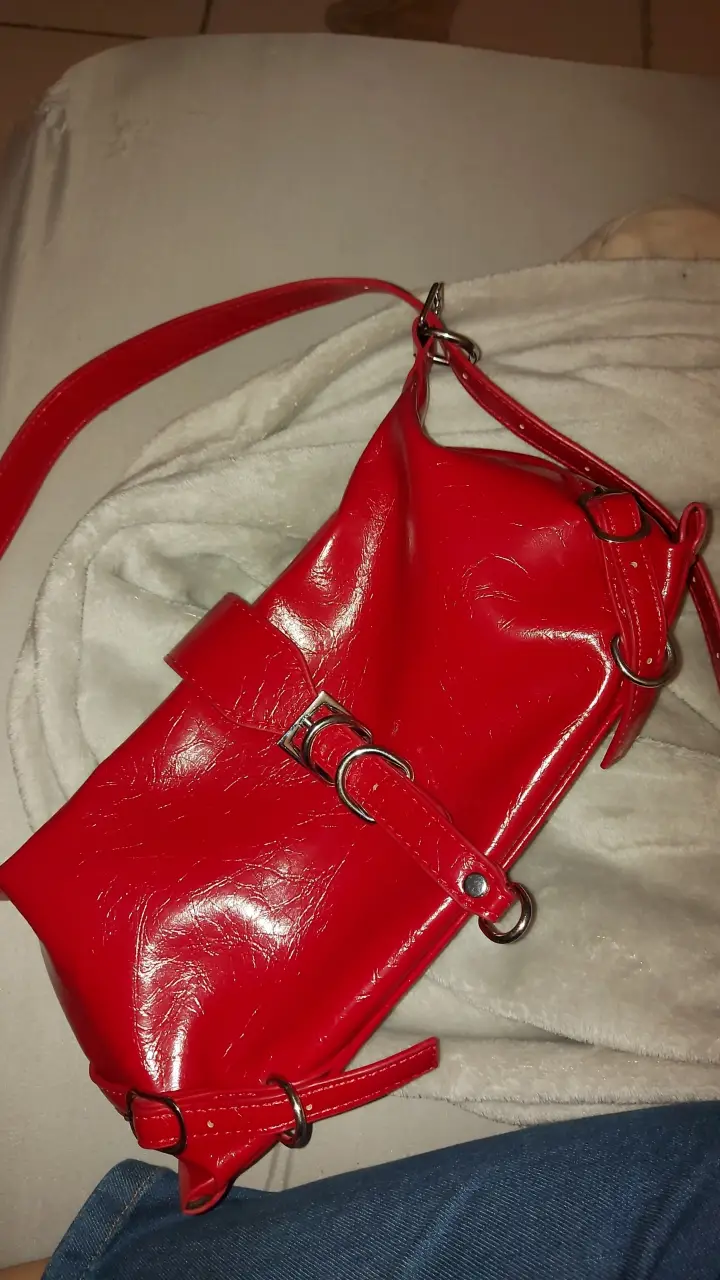Cartera bandolera roja de charol con detalles de hebillas y correa ajustable. Ideal para un look moderno y audaz.